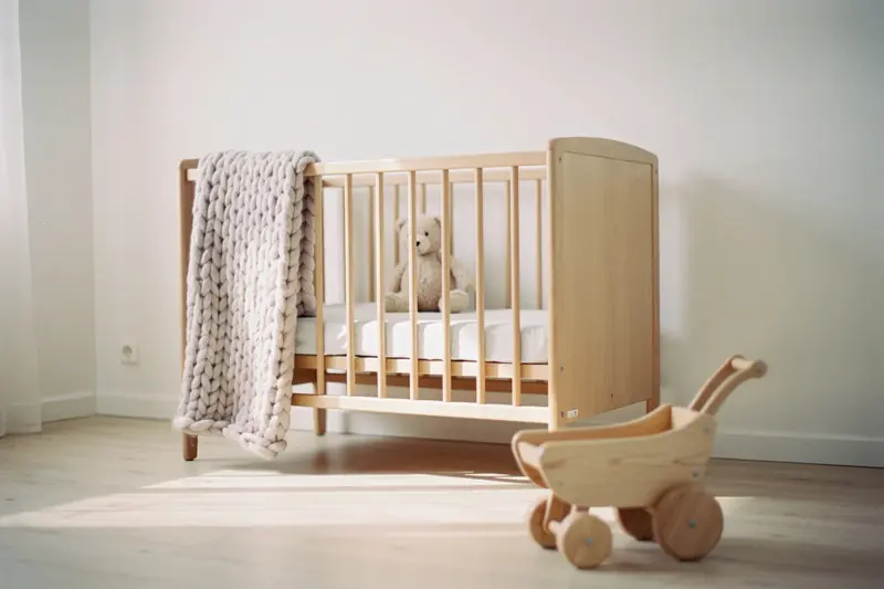 Helles Kinderzimmer mit Babybett aus Holz, Strickdecke und Holzspielzeug